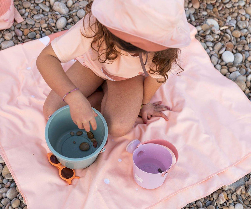 Set spiaggia in plastica bio, Monneka. Bambina che gioca seduta sul telo mare con secchiello ed innaffiatoio variante salvia